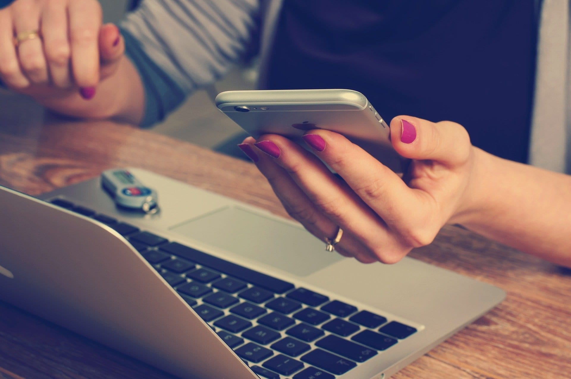 Woman checking mobile phone while working on laptop