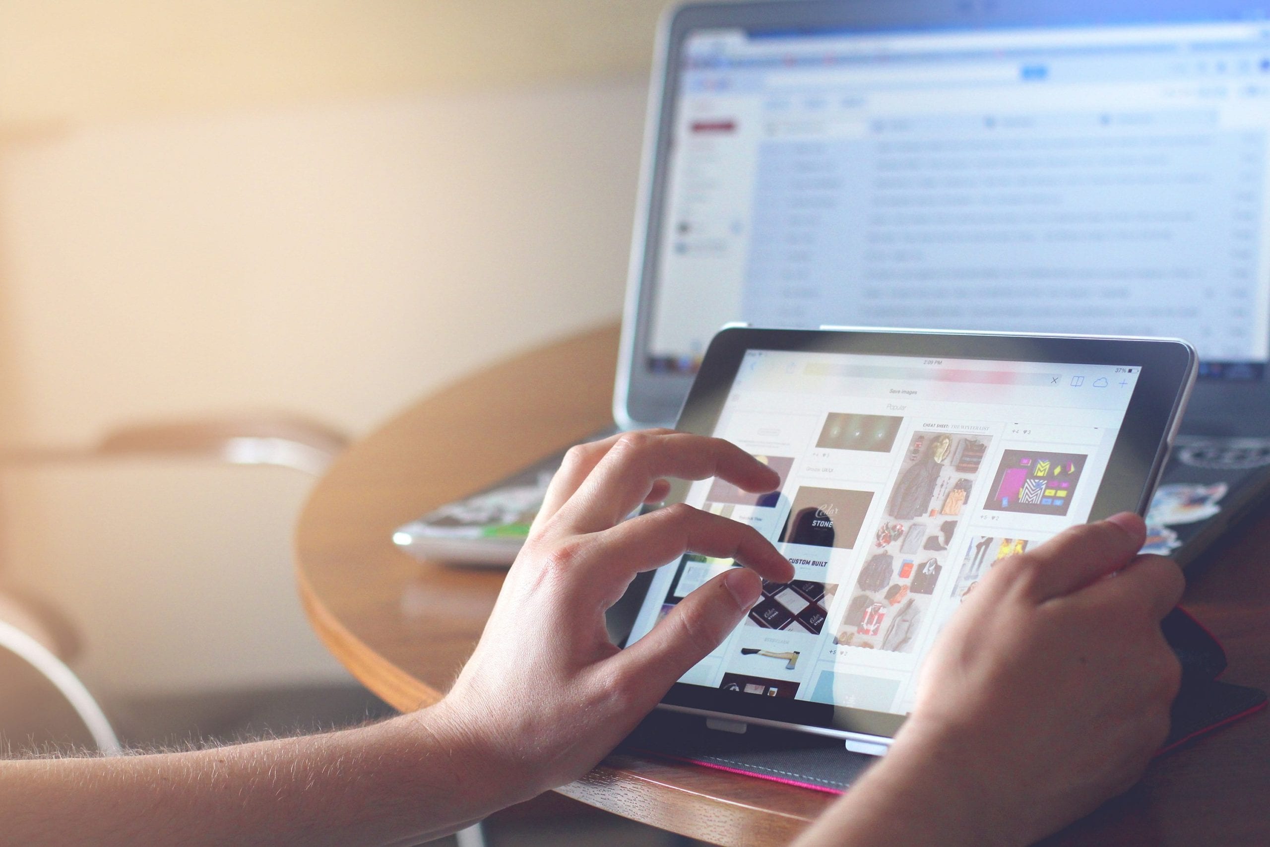 Woman browsing on her iPad with a laptop open in the background